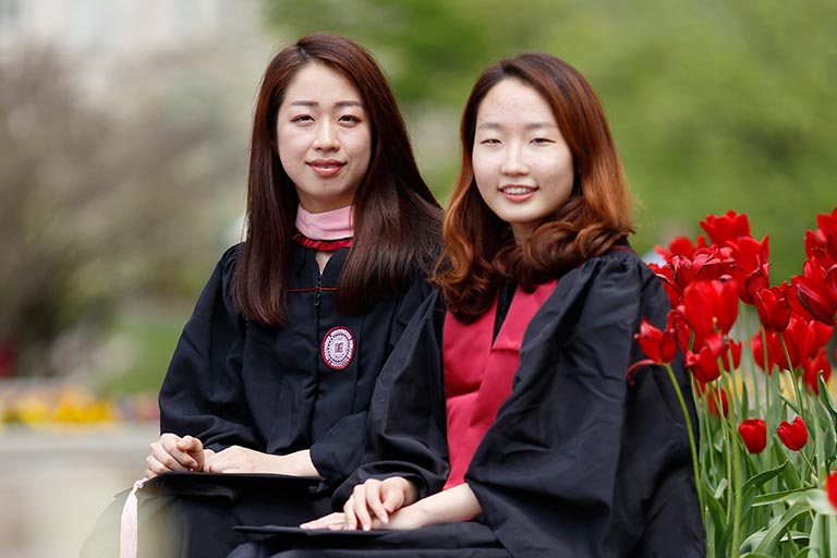two asian american women sitting wearing graduation gowns